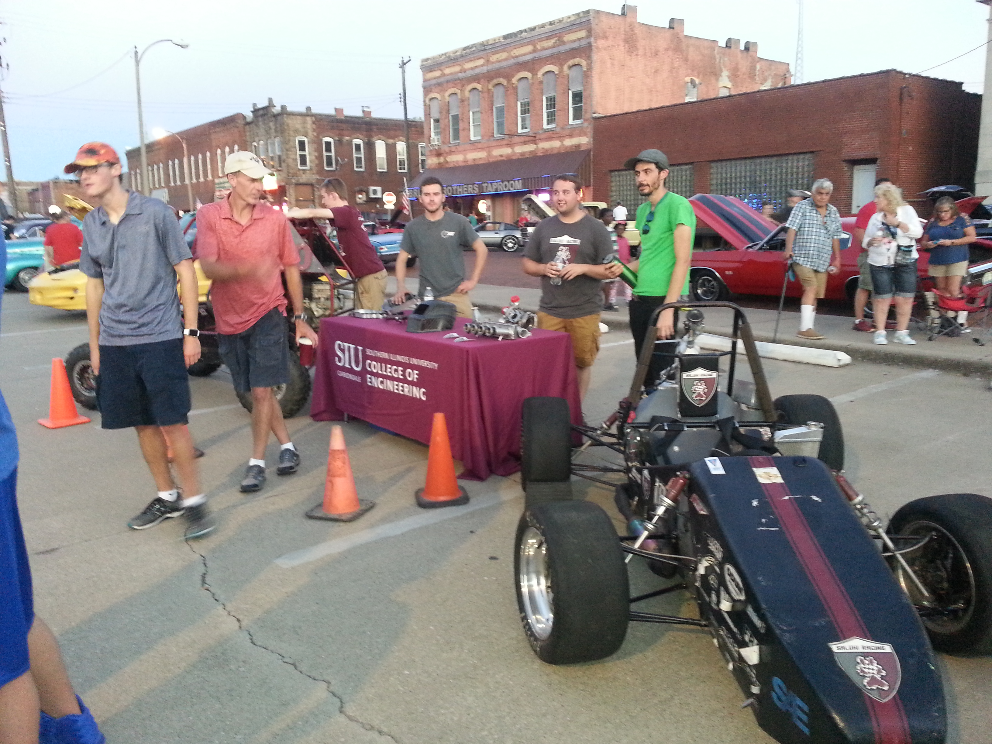 Students at a table next to a Formula 1 style car