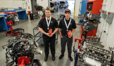 Two students stand in an auto shop, holding awards.