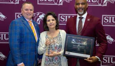 A woman and two men pose for a picture with an award.