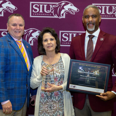 A woman and two men pose for a picture with an award.