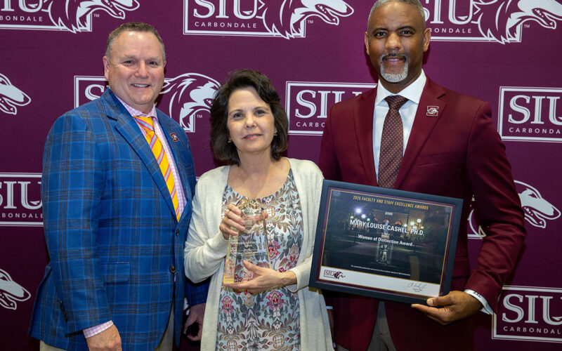 A woman and two men pose for a picture with an award.