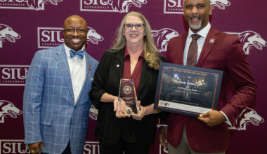 A woman and two men post for a photo after an award ceremony.