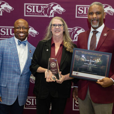 A woman and two men post for a photo after an award ceremony.