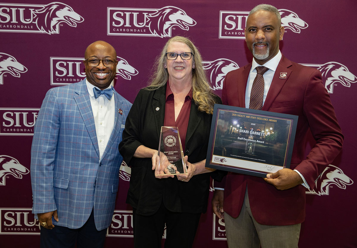 Two men and a woman pose for a picture after an award ceremony.