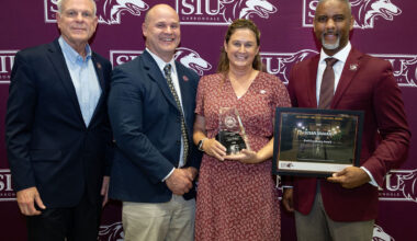 Three men and one woman pose for a photo at an awards ceremony.