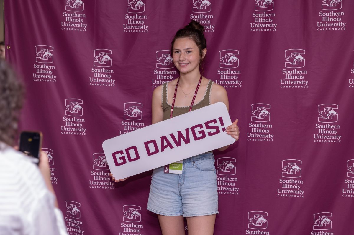 student holding a go dawgs sign while their parent or guardian takes a photo at new student orientation 2026